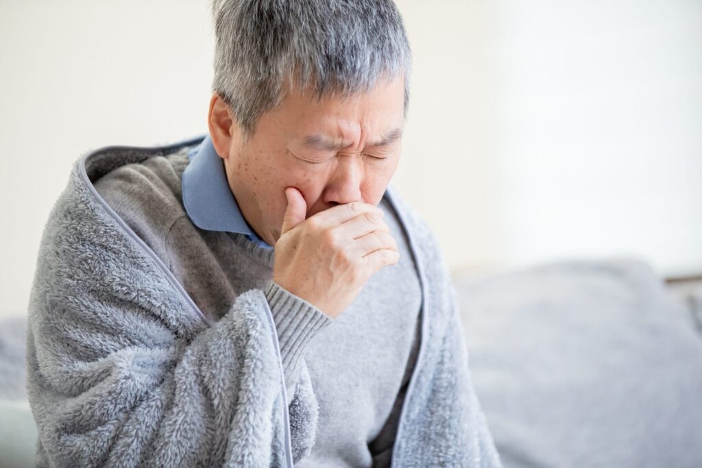 白髪交じりの男性が咳をしている。
