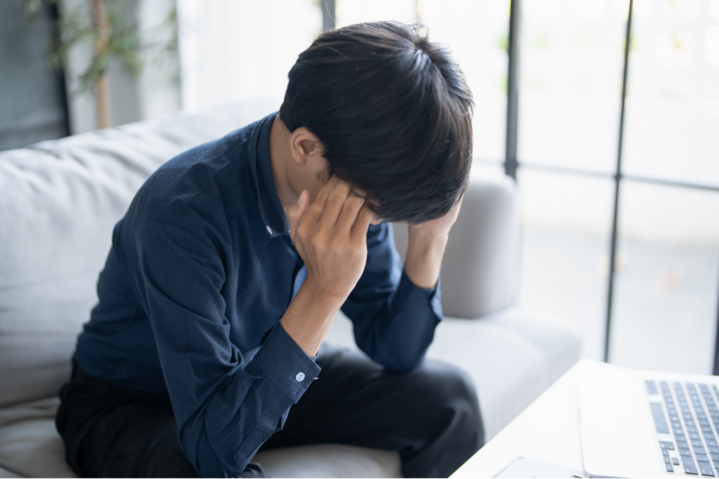 ソファに座り、両手でこめかみあたりを抑えている人
